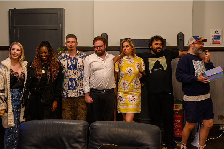 Seven adults stand side by side in a room, posing for a group photo.